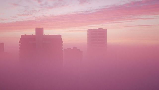 Skyscrapers rising above pink fog in dreamlike cityscape