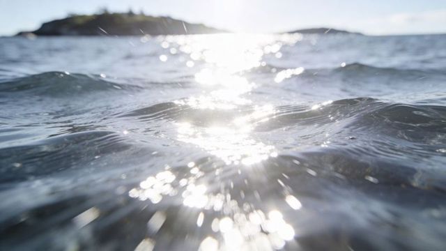 Shimmering sea surface reflecting sunlight over gentle waves near coastal island headland