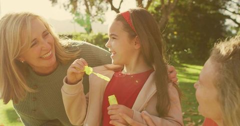 Multigenerational family blowing bubbles in sunlit park, joyful mother and daughter moment