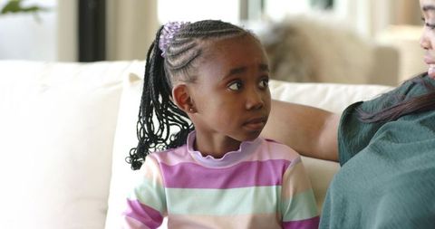 African american mother comforting daughter on couch in pastel striped top, family bonding