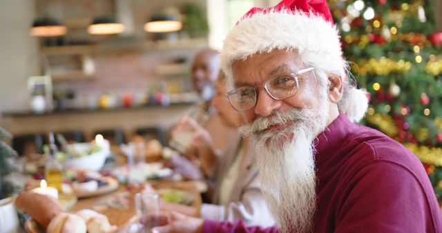 Senior man wearing Santa hat enjoying Christmas meal with family at festive dinner table. Perfect for use in holiday-themed advertisements, family celebration campaigns, or promotional materials highlighting the warmth and joy of Christmas gatherings.