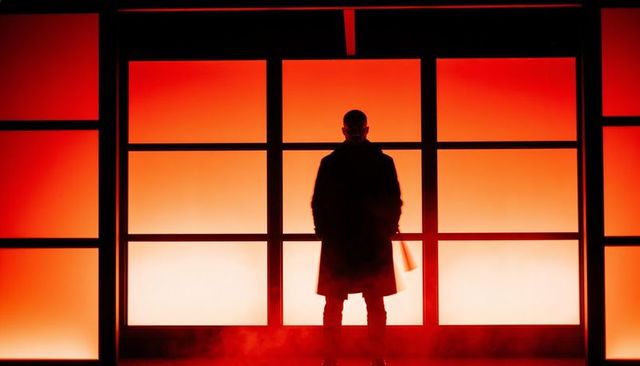 Silhouetted man standing before red backlit panel wall holding briefcase cinematic mood