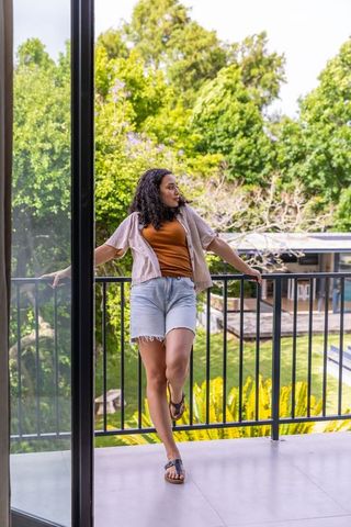 African american woman leaning on balcony railing looking right over lush backyard garden