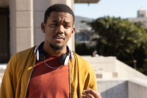 African american man standing on urban terrace wearing mustard jacket and headphones