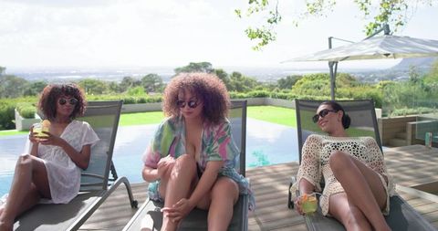 African american friends lounging by infinity pool, applying sunscreen, summer resort