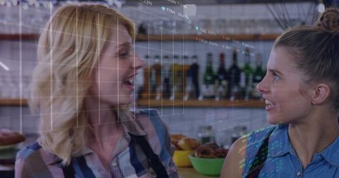 Two baristas chatting behind rustic cafe counter with pastries and digital data overlay