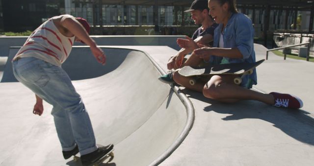 Group of friends enjoying skateboarding in open park. Person skating bowl while friends watch, laugh, and cheer. Perfect for promoting urban outdoor activities, social fun, sporting events, youth culture, motivational scenes.