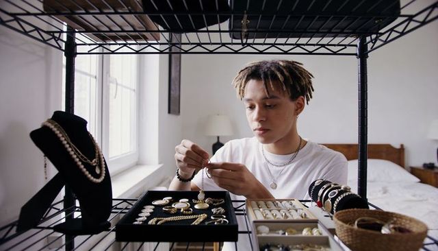 Young jeweler examining pendant at home studio with organized jewelry display