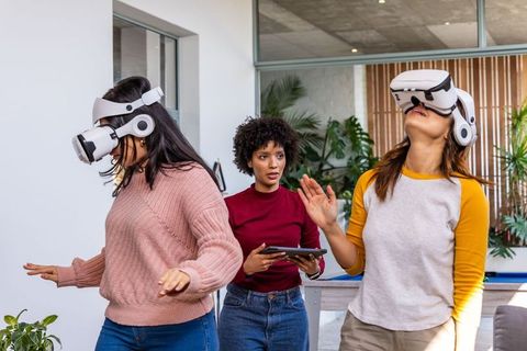 Multicultural women testing vr headsets while guide holding tablet in open office