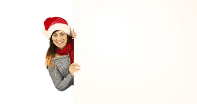 Woman in Santa hat smiling while holding blank white sign suitable for Christmas and holiday greetings, advertisements, and promotional material. Great for use in seasonal marketing, email campaigns, and festive messages.