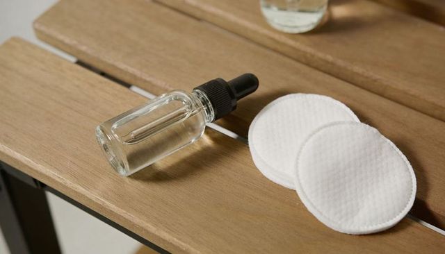 Clear glass dropper bottle with cotton pads on wooden slats, minimal skincare flatlay