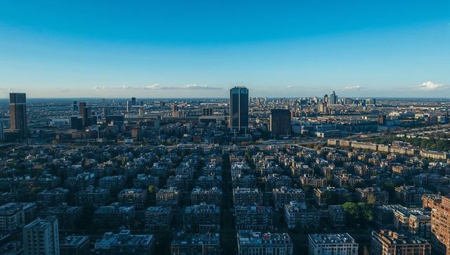 Sunlit aerial cityscape featuring dark rectangular high-rise and street-grid panorama