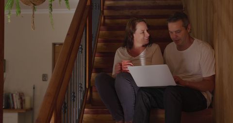 Smiling Couple Using Laptop on Staircase at Home