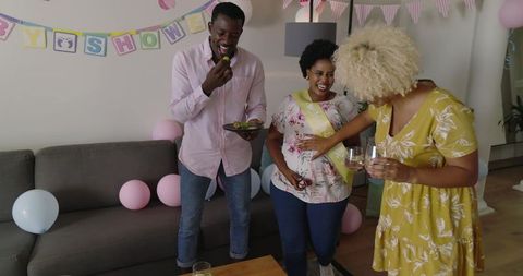 Diverse Friends Celebrating Baby Shower at Home with Mom-to-Be Wearing Yellow Sash