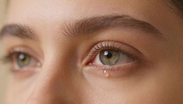 Close-up hazel eye shedding single tear with emotional gaze and natural skin texture