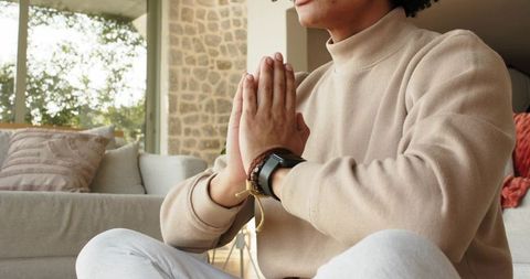 Man practicing mindfulness meditation at home with palms together, cozy sunlight in living room
