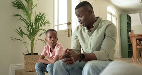 African american father having heartfelt conversation with son in sunlit living room
