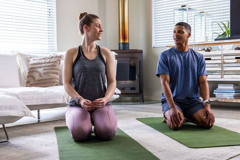 Couple practicing at-home yoga kneeling on mats, chatting and stretching in living room