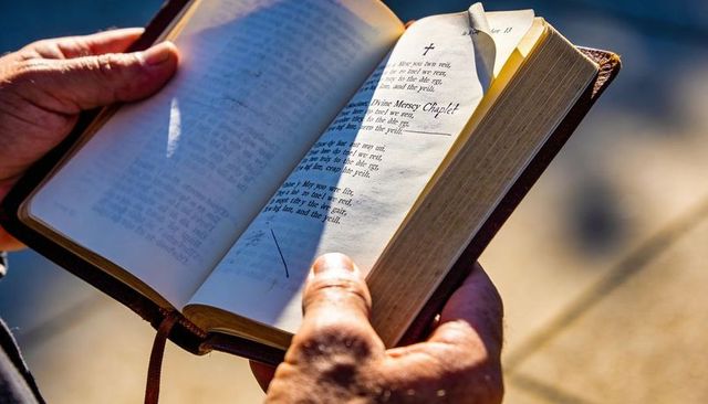 Mature hands holding open leather prayer book in warm sunlight with ribbon bookmark