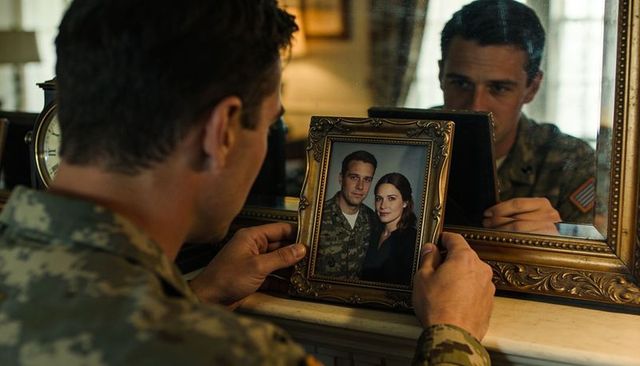 Service member holding ornate frame gazing at portrait on mantel reflecting longing yearning