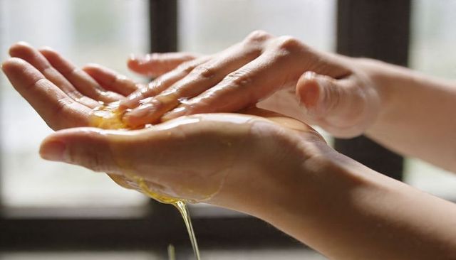 Closeup hands cracking raw egg with yolk dripping over palm and spreading egg white
