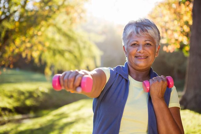 Portrait of smiling mature woman exercising with dumbbell at park