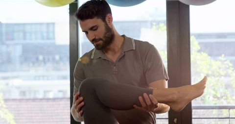 Trainer supporting client leg during rehabilitation stretch in urban studio balcony