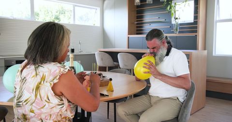 Senior couple preparing for celebration by inflating balloons at home