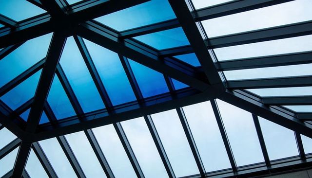 Modern geometric glass skylight atrium with steel trusses and blue tempered panels
