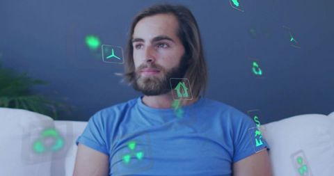 Contemplating bearded man sitting on sofa surrounded by holographic green ar icons