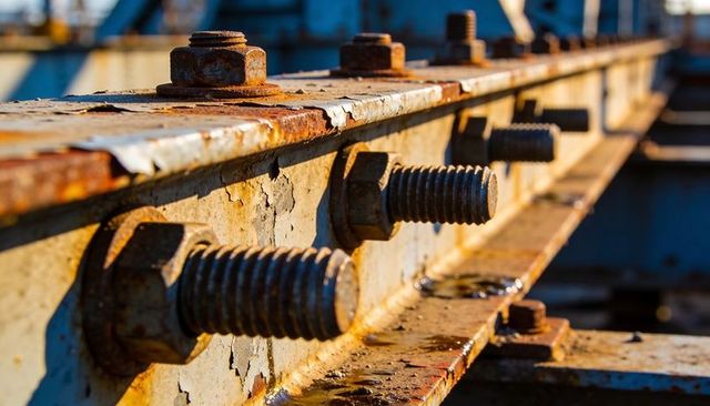 Rusted steel beam showing large threaded bolts on bridge girder with weathered patina