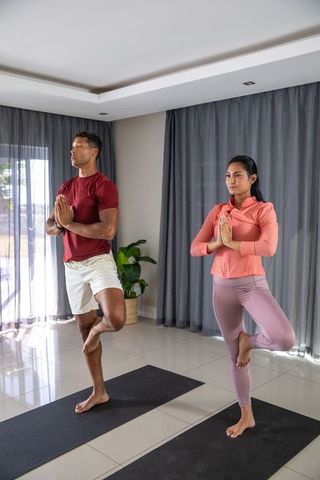 Diverse couple practicing yoga tree pose in modern living room
