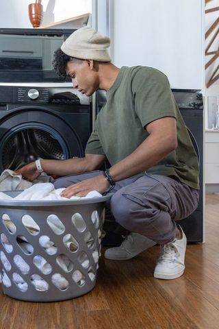 Young african american man loading towels into front-load washer in bright laundry room