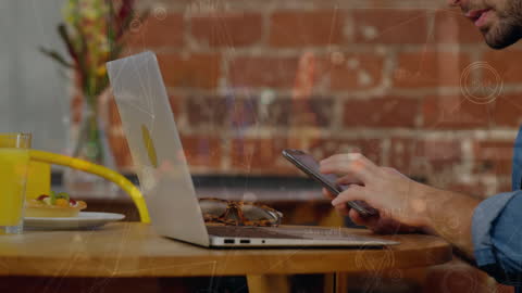 Close-up of Hand Using Smartphone Next to Laptop with Digital Overlay