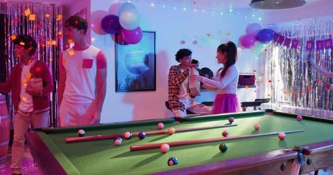 Friends celebrating birthday at disco pool table handing trophy with confetti and balloons
