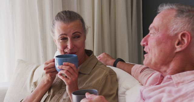 Caucasian senior couple drinking coffee cup while talking to each other sitting on the couch at home. staying at home in self isolation in quarantine lockdown