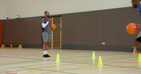 Basketball coach holding basketball coaching dribbling drills on indoor court with cones
