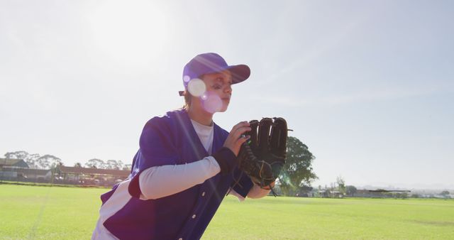 Female athlete in baseball uniform preparing to catch a ball. Useful for sports promotions, athletic training materials, and articles on women in sports. Highlights determination and readiness of the player.
