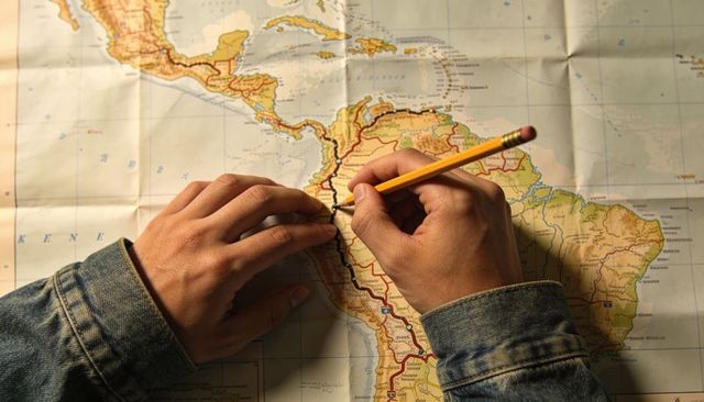 Adult hands tracing route on central america map with pencil and denim jacket sleeves