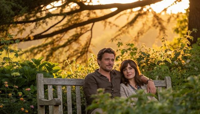 Couple relaxing on weathered wooden garden bench surrounded by lush greenery at golden hour