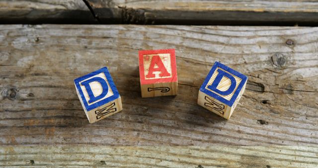 Alphabet blocks spell out DAD on a rustic wooden surface, with copy space. These colorful blocks evoke a sense of childhood and could be used for Father's Day themes or parenting concepts.