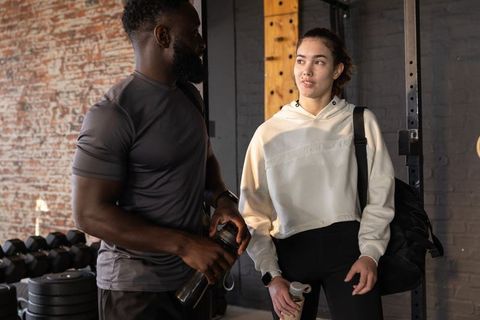 Personal trainer and trainee chatting between sets in industrial gym with shaker bottles