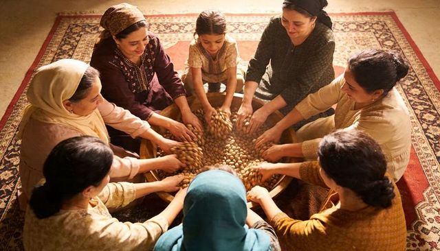 Communal almond sorting: women and girl working around large wooden basin on persian rug