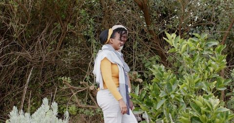 African american couple walking on leafy trail wearing yellow sweater and scarves, candid
