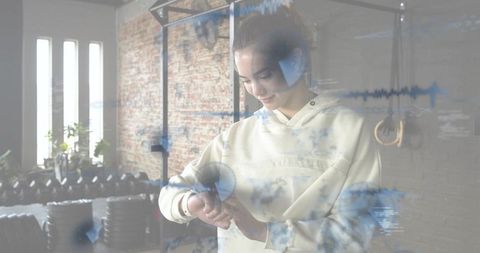 Woman checking smartwatch in industrial gym with digital fitness data overlay