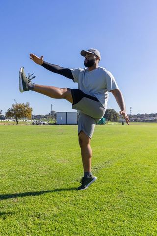 African american athlete performing high kick balancing on one leg in sunny park