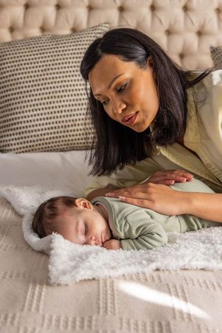 Mother tenderly watching sleeping newborn on cozy bed with soft blanket