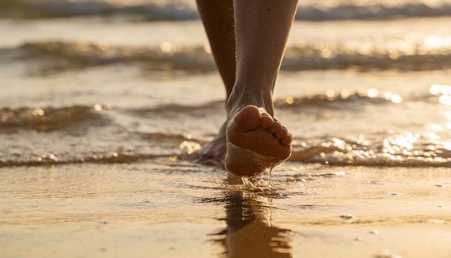 Barefoot walking on wet sand at golden hour with reflected foot and dripping water droplets