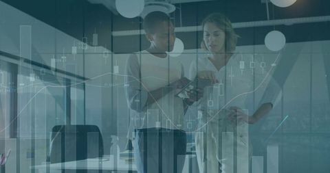 Two colleagues reviewing tablet with financial charts and candlestick graphs in office
