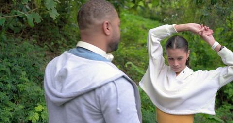 Couple stretching during casual walk in woodland park, woman raising arms, man watching